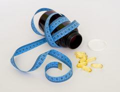 A blue tape measure wrapped around a pill container with some pills laying next to it